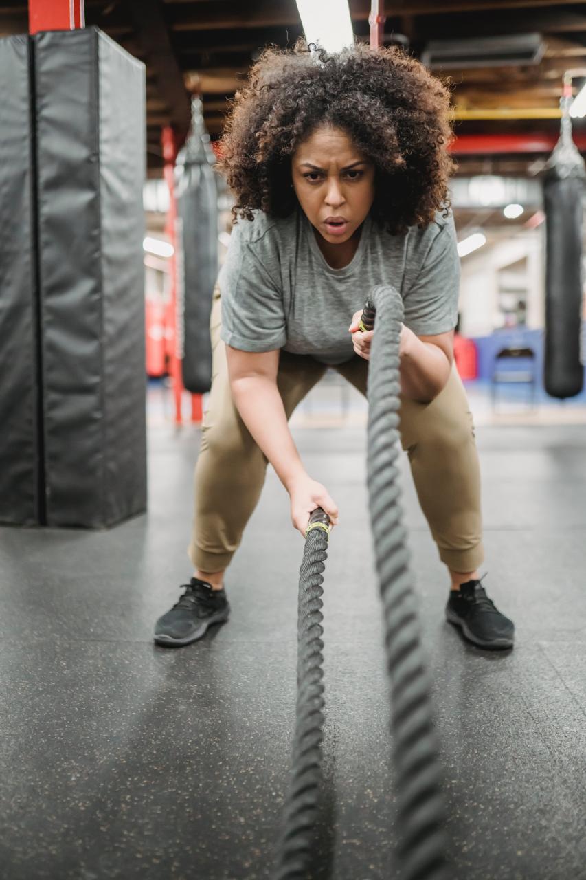 Strong obese black woman exercising with heavy ropes in gym